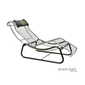 May include: A modern chaise lounge with a black metal frame and a silver wire seat. The headrest is a small, dark pillow. The words "QUALITY IS KEY decor" are printed in black at the bottom right.