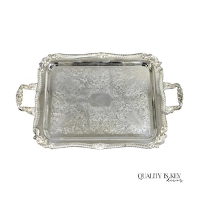 May include: A rectangular silver serving tray with ornate floral and scrollwork detailing. The tray has two handles and a decorative border. The words "QUALITY IS KEY decor" are in the bottom right corner.