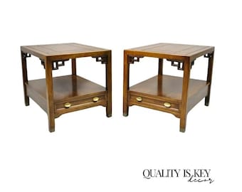 May include: Two matching wooden side tables with a dark brown finish. Each table has a rectangular top, a lower shelf, and a drawer with a brass knob. The tables have decorative corner brackets and are set against a white background. The text "QUALITY IS KEY decor" is at the bottom.