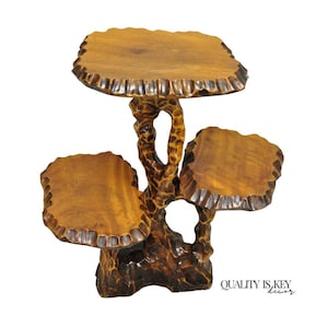 May include: A three-tiered wooden plant stand with a natural, tree-like design. The stand features three circular platforms of varying sizes, supported by a carved, textured trunk. The wood has a warm, brown tone with darker accents.