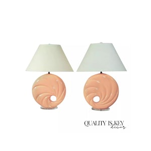 May include: A pair of table lamps with peach-colored ceramic bases shaped like a swirl. The bases have a hole in the center. The lamps have white drum shades.