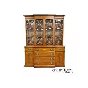 May include: A large, antique wooden hutch with glass doors and drawers. The hutch has a rich, dark brown finish and intricate details. The glass doors are framed with ornate wood and feature a geometric pattern. The hutch has a total of six drawers, with two on the top and four on the bottom. The hutch is a beautiful piece of furniture that would be a great addition to any home.