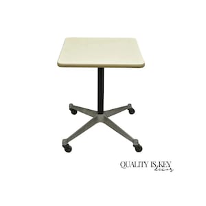 May include: A small, square, cream-colored table with a black central support and a silver-colored, star-shaped base with wheels. The table is designed for mobility and convenience. The text "QUALITY IS KEY decor" is in the lower right corner.