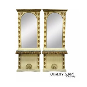 May include: A pair of antique white and gold painted mirrors with ornate frames and a marble top. The mirrors have a scalloped design and are accented with gold leaf.