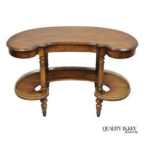 May include: A kidney-shaped, wooden side table with a dark brown finish. The table features two semi-circular shelves with brass trim and decorative legs. The top surface has a curved design with rounded edges. The table is a classic piece of furniture.