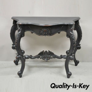 May include: A black wooden console table with ornate carvings and scrolled legs. The table has a curved top and a distressed finish.