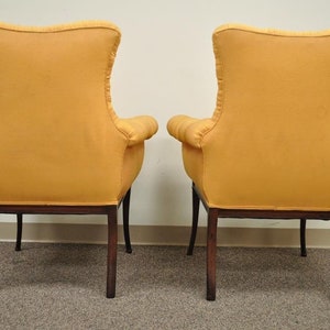 May include: A pair of yellow upholstered armchairs with dark wood legs. The chairs are facing away from the camera, showing the back of the chairs.