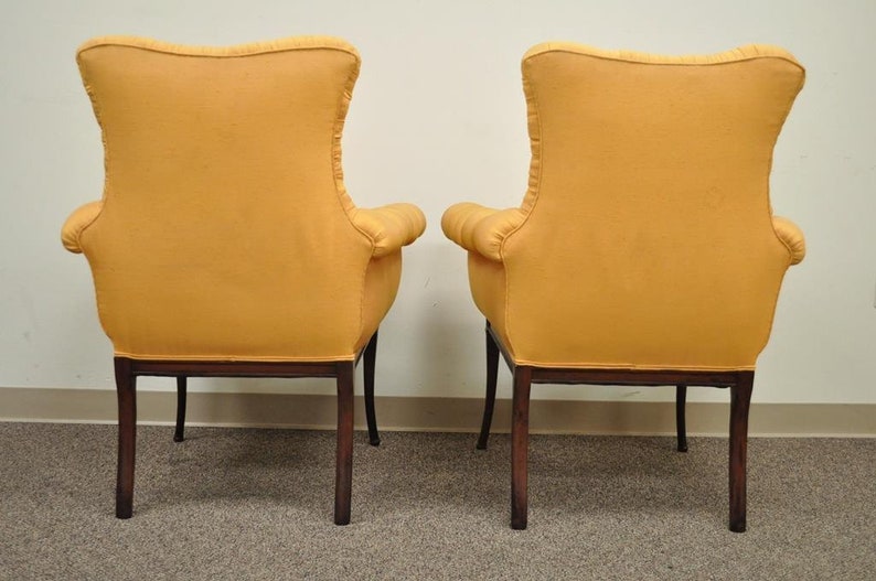 May include: A pair of yellow upholstered armchairs with dark wood legs. The chairs are facing away from the camera, showing the back of the chairs.