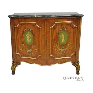 May include: A wooden cabinet with a black marble top. The cabinet doors feature oval green and gold painted panels with a figure. Floral and gold accents adorn the cabinet. The text "QUALITY IS KEY decor" is at the bottom.