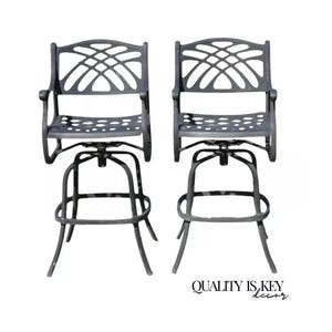 May include: Two black metal swivel bar stools with an intricate, openwork design on the back and seat. The stools have a round base with a footrest.