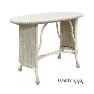 May include: White wicker oval table with a white top and intricate woven details. The table has a unique design with curved legs and a woven base.