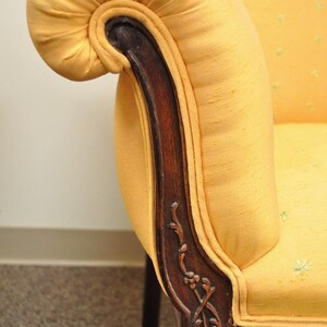 May include: A yellow fabric armchair with a carved wooden armrest and a scrolled design. The chair has a tufted back and a rolled armrest.