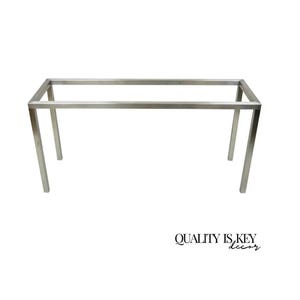 May include: A rectangular, silver-colored metal table frame with four legs. The frame is made of square tubing and has a minimalist design. The text "QUALITY IS KEY decor" is in the bottom right corner.
