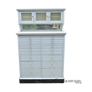 May include: A light blue antique cabinet with multiple drawers and glass-paned doors. The cabinet has a top section with three glass-paned doors and a mirrored shelf. The drawers have crystal knobs. The cabinet is a vintage piece of furniture.