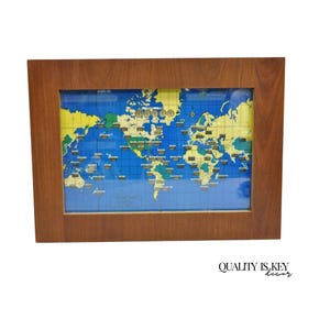 May include: A framed world map with a wooden frame. The map features a blue ocean, yellow landmasses, and small gold-colored pins marking locations. The text "QUALITY IS KEY decor" is in the bottom right corner.