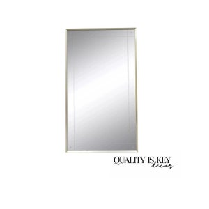 May include: A large, rectangular mirror with a gold frame. The frame has a decorative design with a subtle pattern. The mirror is reflecting a white wall.