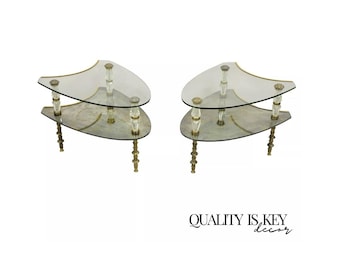 May include: A pair of mid-century modern glass and brass side tables with a unique triangular shape. The tables have two tiers and feature a mirrored glass top.