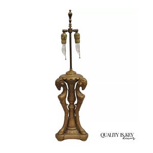 May include: A gold-toned table lamp with a decorative base featuring two stylized animal figures. The lamp has a single light bulb and a chain pull switch.