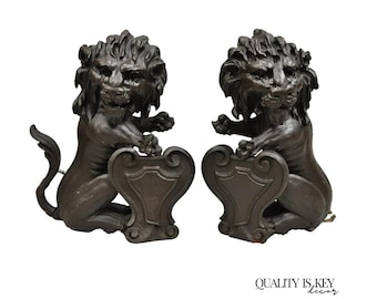 May include: A pair of bronze-colored lion statues, each seated and holding a shield. The lions have detailed manes and are positioned facing forward. The statues are decorative and have a classic design.