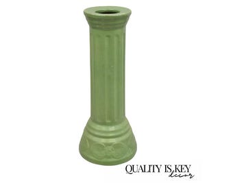 May include: A light green ceramic pillar-shaped decorative item. The pillar has a fluted design and a detailed base with floral accents. The top has a small opening. The words "QUALITY IS KEY decor" are printed in black.