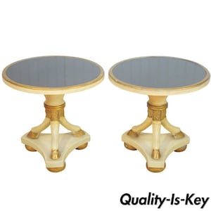 May include: A pair of round, white end tables with gold accents. Each table has a black mirrored top and three legs with gold feet.