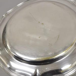 Puede incluir: Una fuente de servir de plata con un borde festoneado. La fuente es redonda y tiene un acabado brillante.