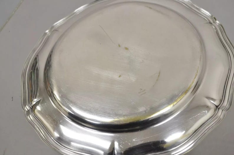 Puede incluir: Una fuente de servir de plata con un borde festoneado. La fuente es redonda y tiene un acabado brillante.