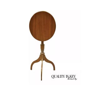 May include: A round, wooden side table with a dark brown finish. The table has a pedestal base with three curved legs. The tabletop is approximately 24 inches in diameter. The text "QUALITY IS KEY decor" is visible.