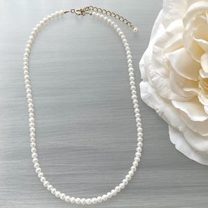 May include: A simple white pearl necklace with a gold clasp.