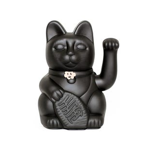Könnte beinhalten: Schwarze Maneki Neko Katzenfigur mit erhobener Pfote, ein traditionelles japanisches Symbol für Glück und Wohlstand. Die Katze hält einen fischförmigen Gegenstand und trägt ein Halsband mit einem blütenförmigen Anhänger.