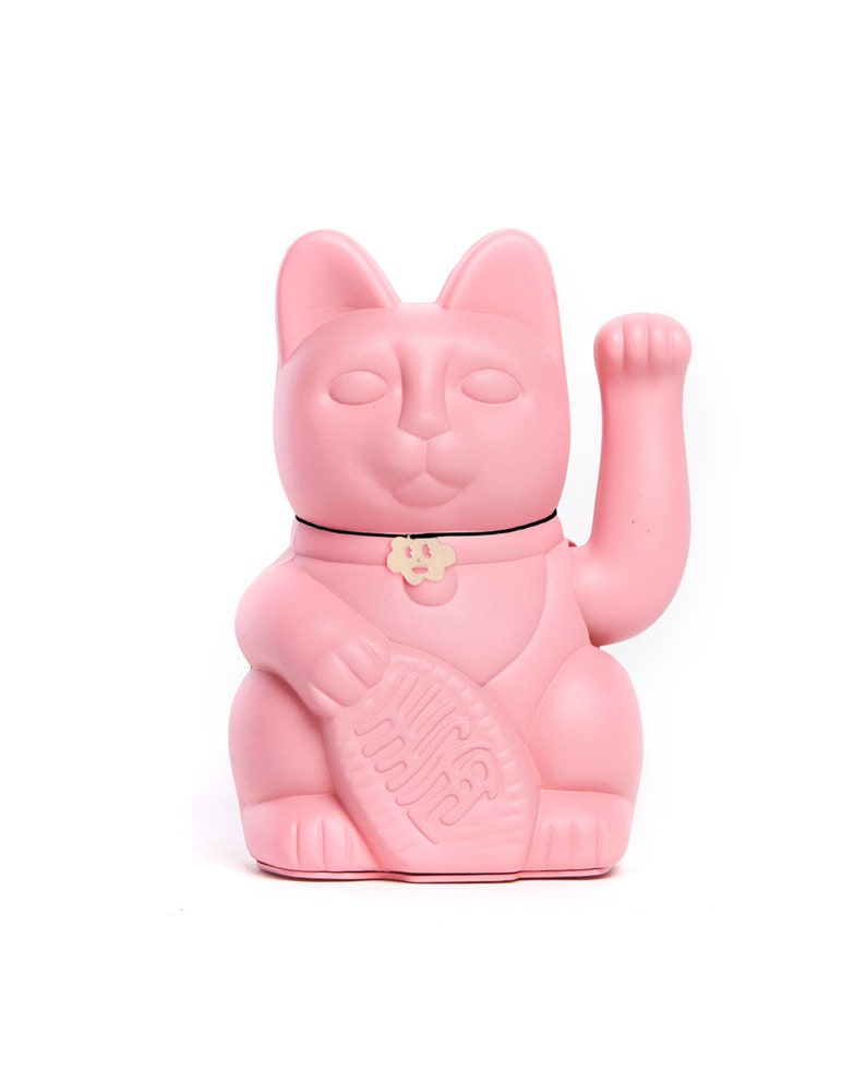 May include: A pink ceramic Maneki-Neko, or lucky cat, with its right paw raised. The cat has a black collar with a gold charm and is holding a gold coin in its left paw.