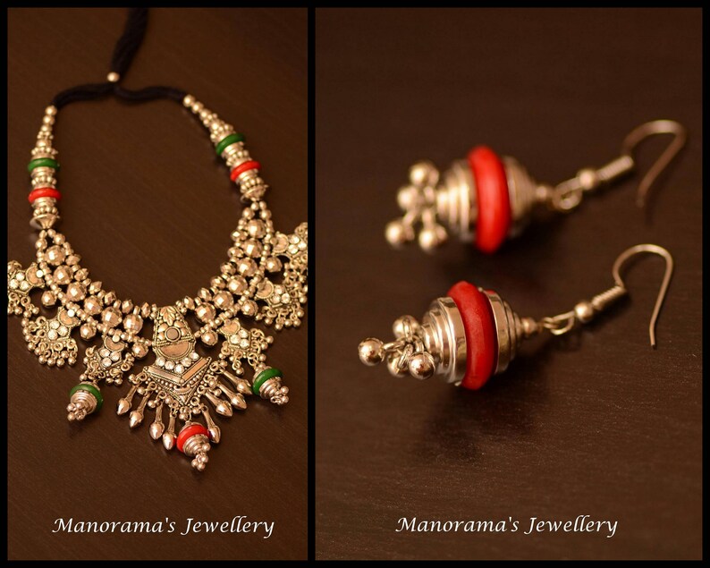 May include: A silver necklace with red and green beads and a silver pendant. The necklace is on a brown surface. Two silver earrings with red beads are also shown.
