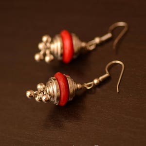 May include: A pair of silver earrings with red bead accents. The earrings have a hook closure and a dangling design.