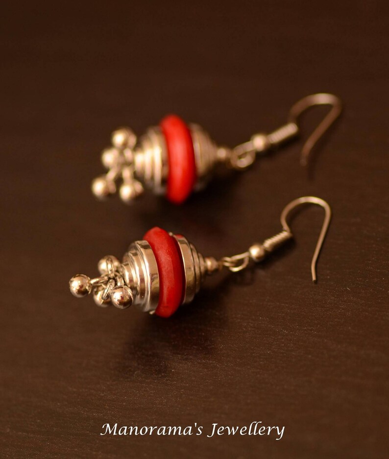 May include: A pair of silver earrings with red bead accents. The earrings have a hook closure and a dangling design.