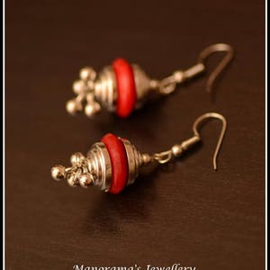 May include: A pair of silver earrings with red and silver round beads. The earrings have a dangling design with a small loop at the top.