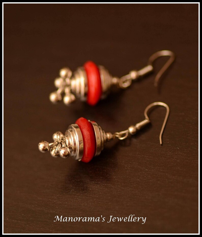 May include: A pair of silver earrings with red and silver round beads. The earrings have a dangling design with a small loop at the top.