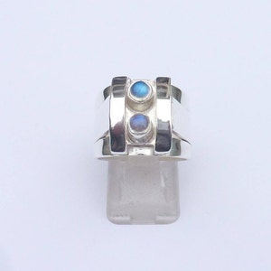 Peut inclure: Une bague en argent avec deux pierres de lune bleues serties dans un motif géométrique.