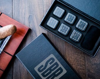 May include: A set of six black whiskey stones in a black box with the letters "SBR" on the box and the stones. The stones are in a black velvet pouch. The box is open and the stones are visible.