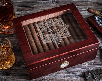 May include: A mahogany wood cigar humidor with a glass top and a brass clock on the front. The humidor is filled with cigars and has an engraved monogram "SWS" on the glass top.