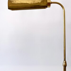 Puede incluir: Una l&aacute;mpara de pie vintage de lat&oacute;n con una pantalla rectangular y un brazo curvo. La l&aacute;mpara tiene un tono dorado c&aacute;lido y un dise&ntilde;o cl&aacute;sico. La altura de la l&aacute;mpara es de aproximadamente 152 cm.