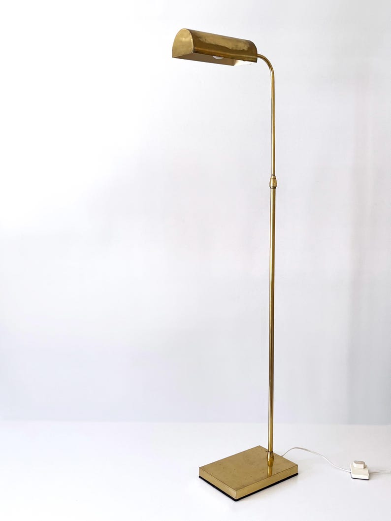 Puede incluir: L&aacute;mpara de pie vintage de lat&oacute;n con base rectangular y pantalla curva. La l&aacute;mpara tiene un tallo delgado y ajustable y un interruptor de encendido/apagado simple. La l&aacute;mpara es de color dorado c&aacute;lido y est&aacute; sobre un fondo blanco.