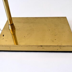 Puede incluir: Base de l&aacute;mpara de escritorio vintage de lat&oacute;n, de forma rectangular. La base tiene un acabado dorado, una parte inferior negra y un v&aacute;stago dorado. Se ve un cable el&eacute;ctrico blanco.