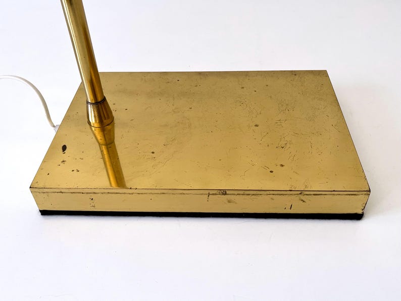 Puede incluir: Base de l&aacute;mpara de escritorio vintage de lat&oacute;n, de forma rectangular. La base tiene un acabado dorado, una parte inferior negra y un v&aacute;stago dorado. Se ve un cable el&eacute;ctrico blanco.