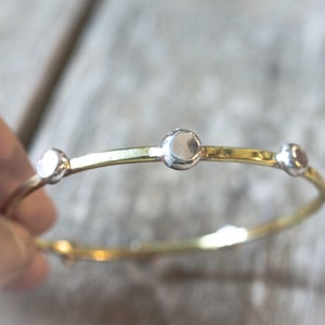 May include: A gold bangle bracelet with three silver round accents.
