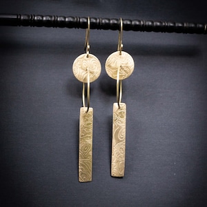 May include: A pair of gold earrings with a circular design and a long, rectangular dangle. The earrings have a textured, swirling pattern.