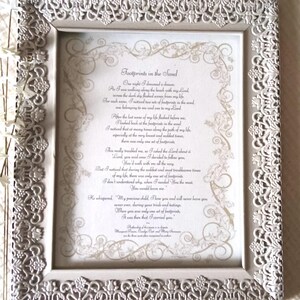 May include: A framed print with the poem "Footprints in the Sand." The white frame has a delicate, ornate design. The poem is in a script font with decorative flourishes.