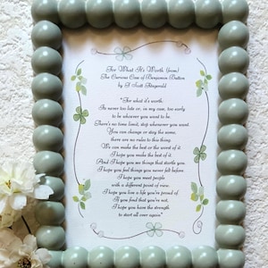 May include: A rectangular picture frame with a sage green beaded border containing a printed quote from The Curious Case of Benjamin Button by F. Scott Fitzgerald. The text is centred on a white background with delicate green leaf illustrations.