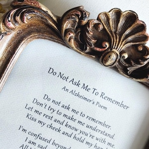 May include: An ornate, antique-style bronze picture frame with intricate scrollwork and shell detailing at the top. Inside the frame is a white card printed with the poem Do Not Ask Me To Remember, An Alzheimer's Poem, in black Gabriola font.