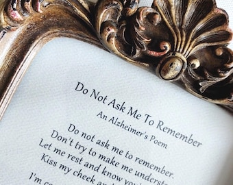 May include: An ornate, antique-style bronze picture frame with intricate scrollwork and shell detailing at the top. Inside the frame is a white card printed with the poem Do Not Ask Me To Remember, An Alzheimer's Poem, in black Gabriola font.