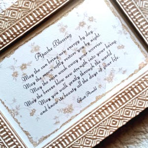 May include: A rectangular picture frame with a textured gold finish containing a white card with the Apache Blessing poem printed in black script. The card features a faint floral pattern and a decorative gold border around the text.